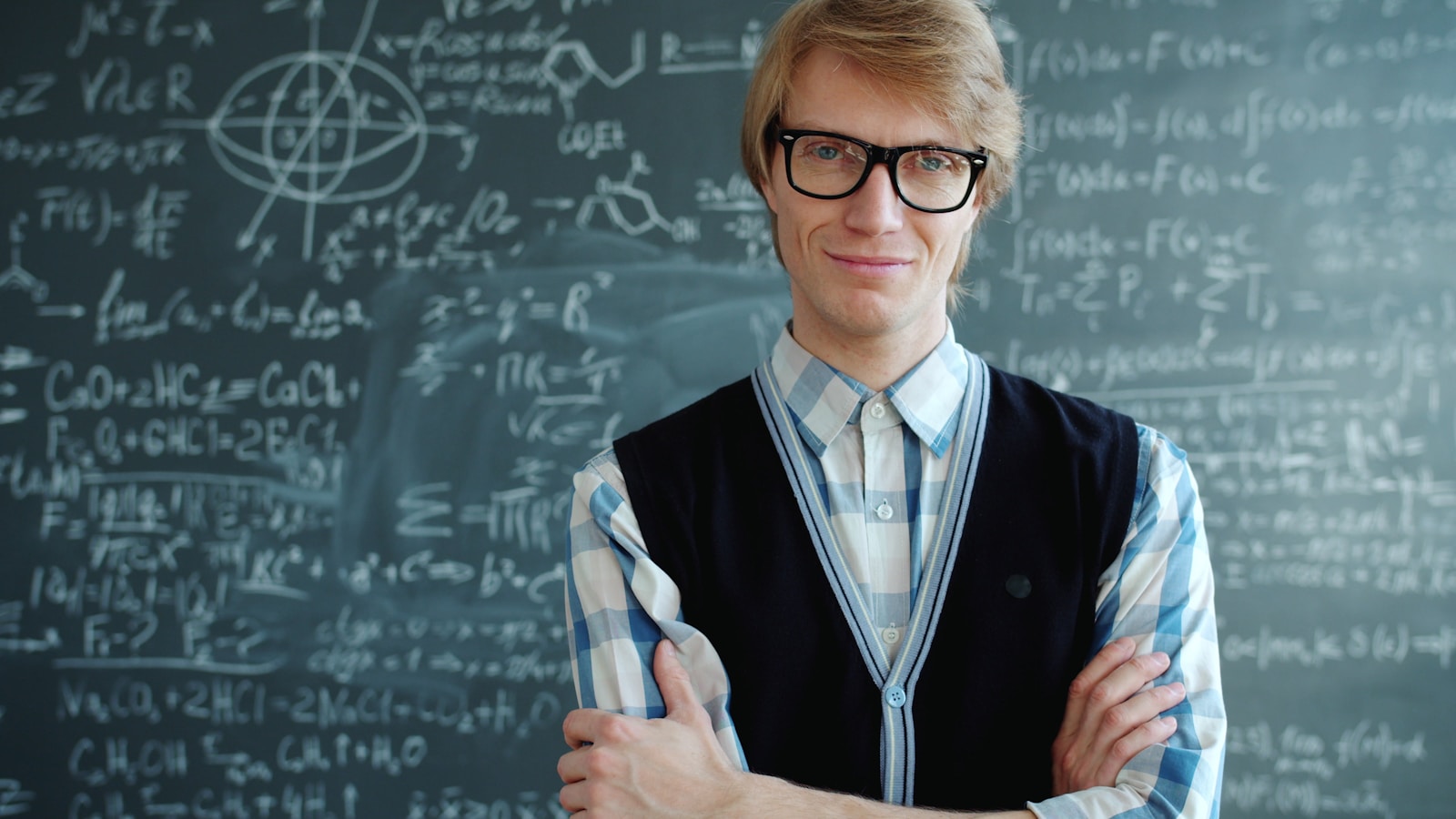 Man in glasses stands by chalkboard with math equations